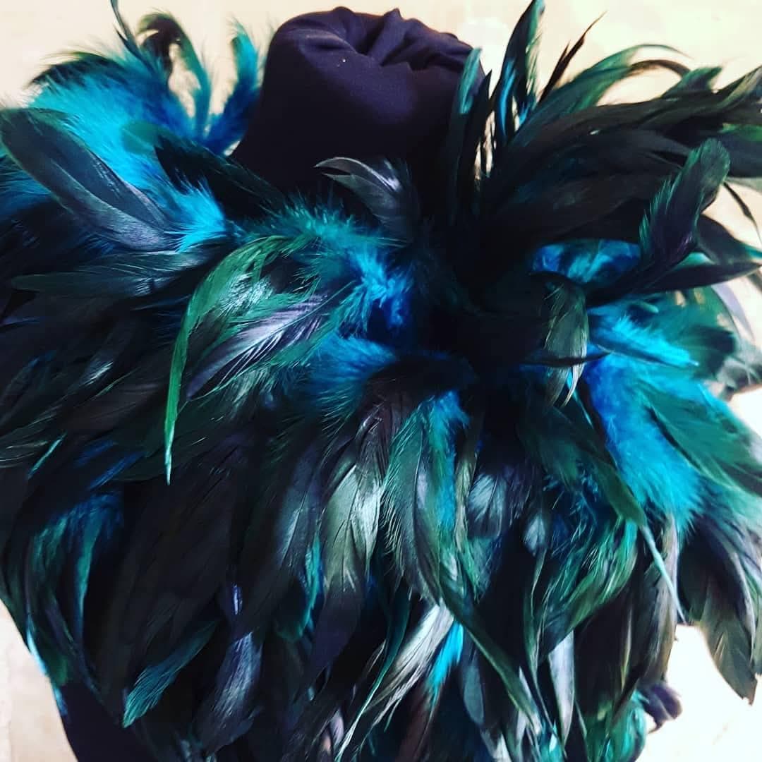 Accessoire composé de plumes bleues, turquoise et vertes autour d’une fleur violette.