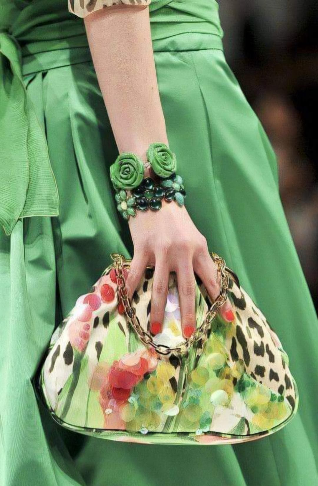 Détail d’une robe verte, d’un bracelet à fleurs et perles et d’un sac multicolore à chaîne dorée.