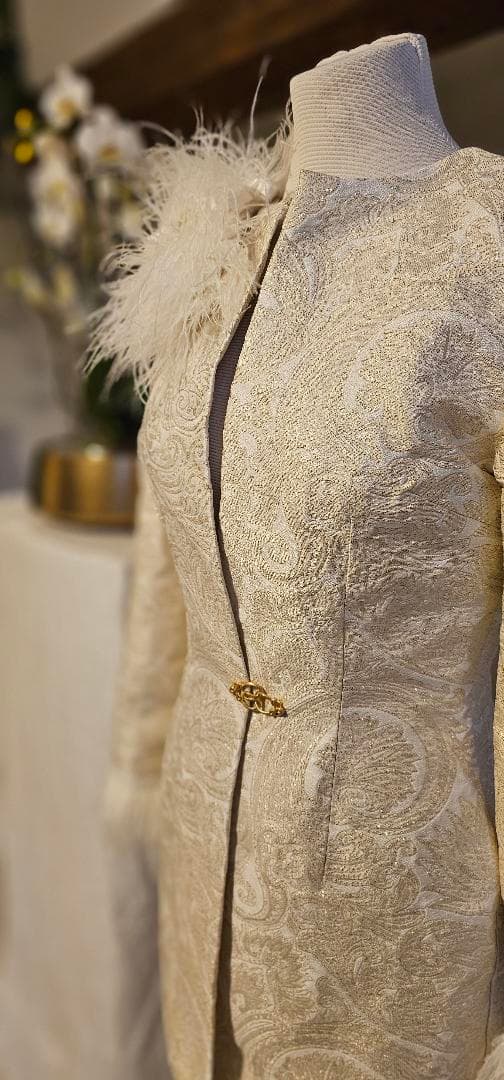 Veste ivoire à motifs et plumes, présentée sur un mannequin dans l’atelier.