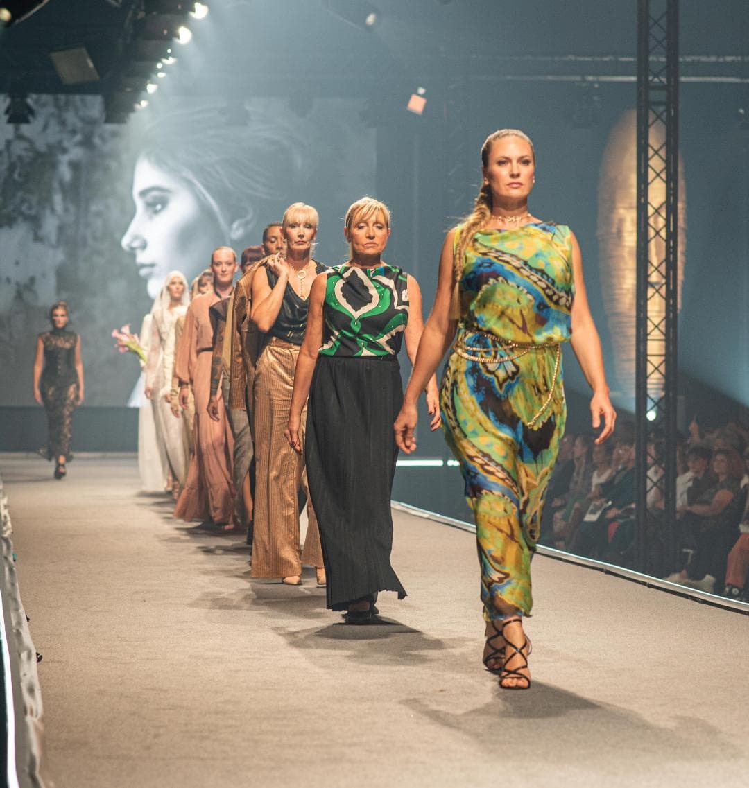 Final d’un défilé avec plusieurs mannequins portant des tenues aux matières et imprimés variés.