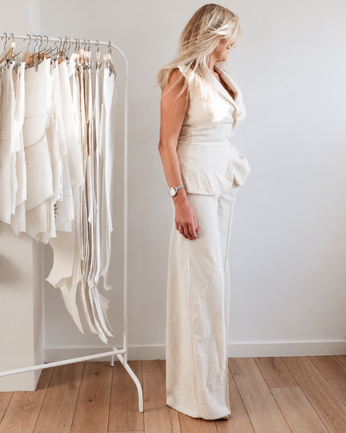 Silhouette en gilet et pantalon large ivoire, devant un portant de patrons à l’atelier.