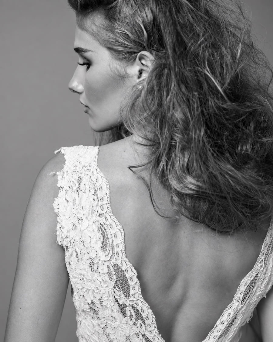Portrait de dos d’une mariée en robe de dentelle, photographie en noir et blanc.